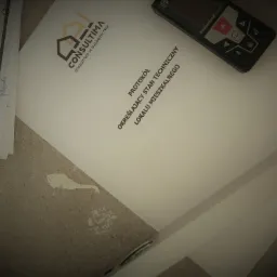 Protokół techniczny lokalu mieszkalnego z logo firmy Consultima, plan mieszkania z naniesionymi wymiarami i dalmierz laserowy Bosch na szorstkim tle podłoża.