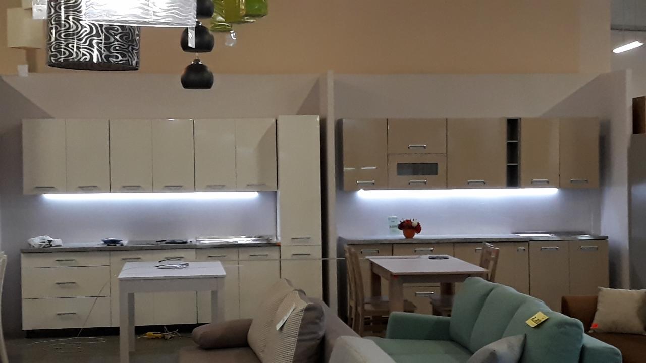 Dwie zabudowy kuchenne z podświetleniem LED podszafkowym, widoczne z perspektywy salonu, z lampami wiszącymi nad nimi.