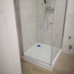 REMKOM SP z O.O. - Nowoczesna kabina prysznicowa z geometrycznym wzorem na płytkach, zamontowana w narożniku łazienki, widoczny odpływ z niebieskim akcentem