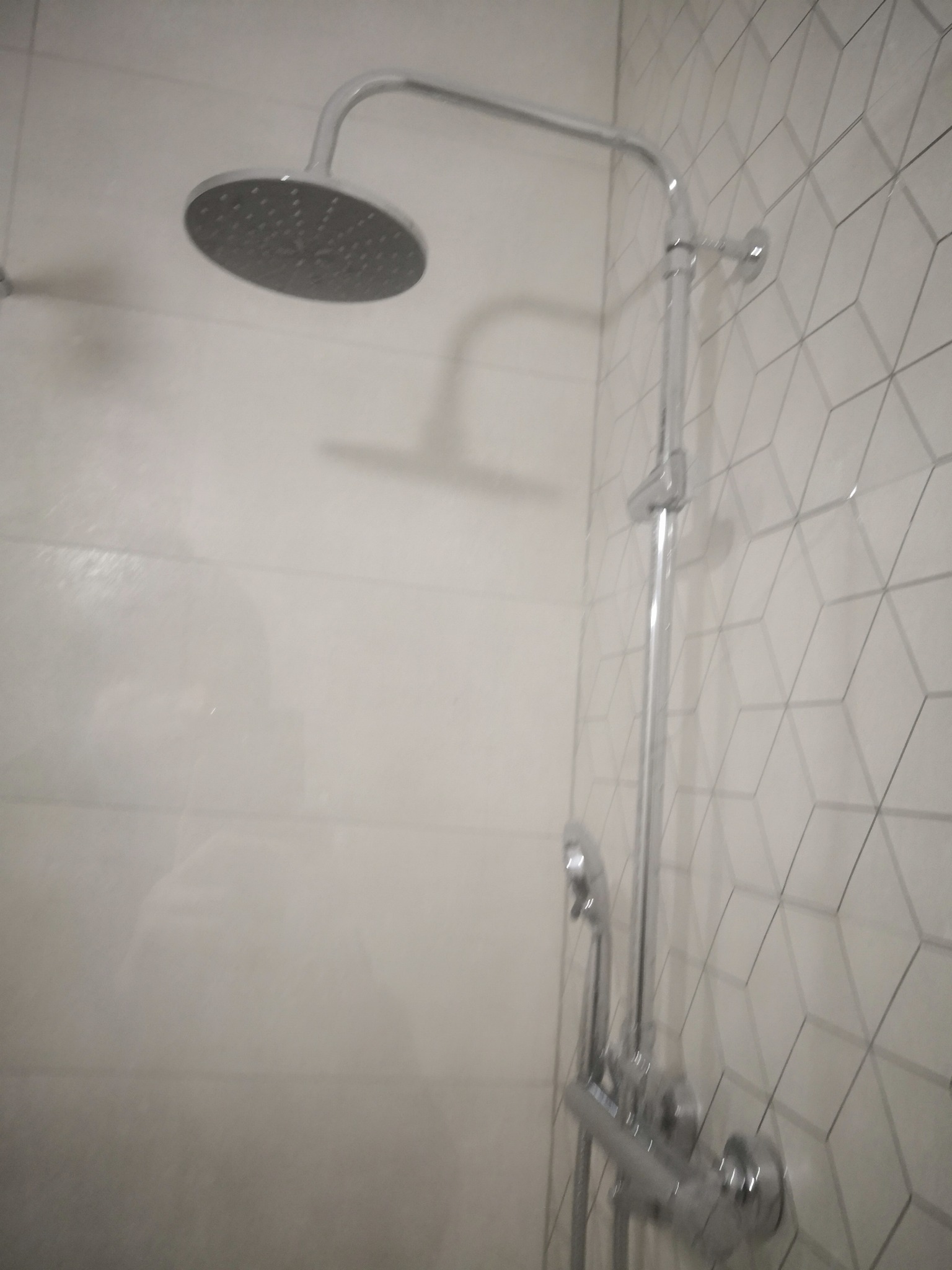 Zamontowany chromowany panel prysznicowy z deszczownicą na tle białych płytek z geometrycznym wzorem w łazience.