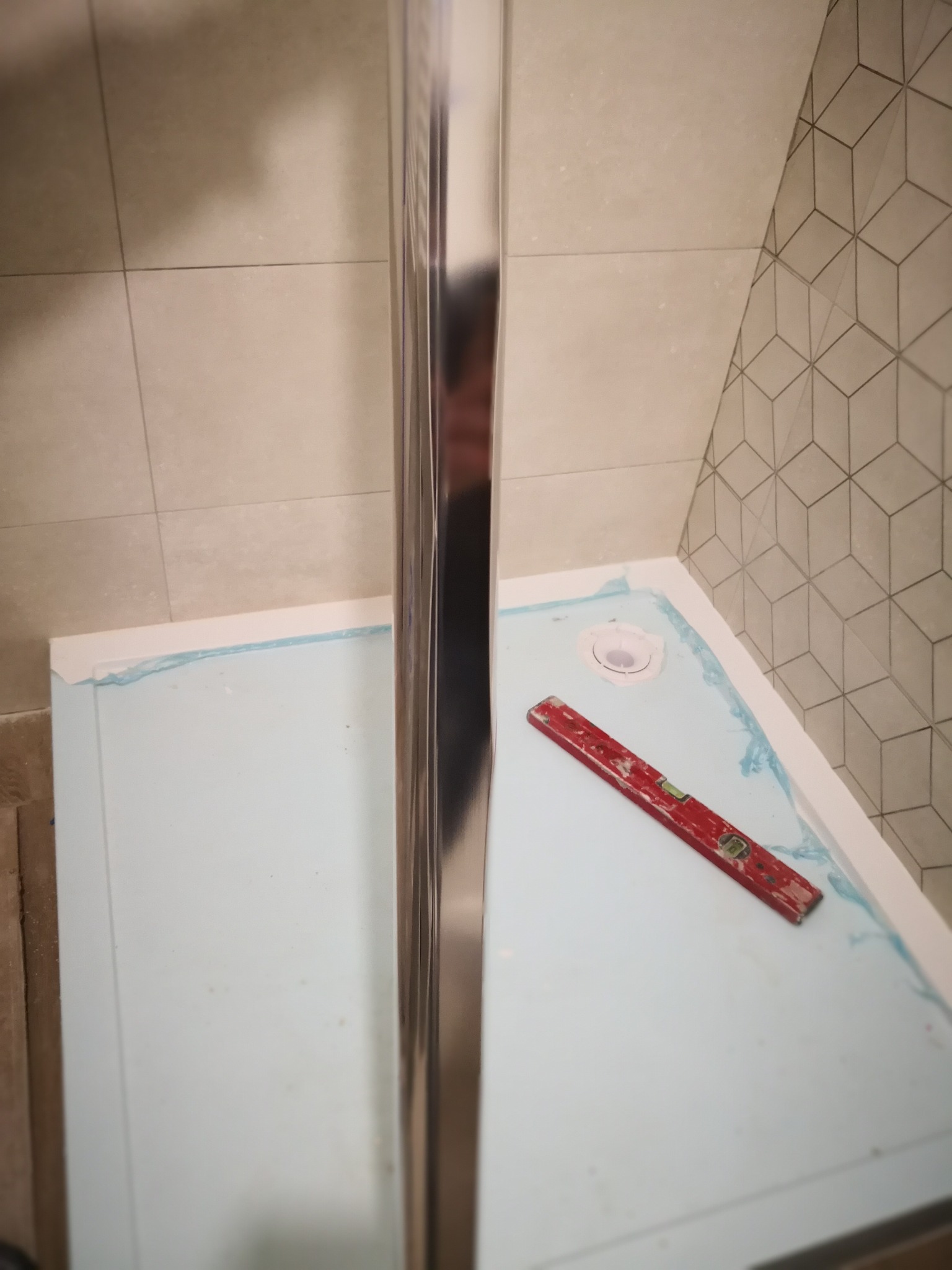 Przygotowanie brodzika kabiny prysznicowej z użyciem poziomicy; zabezpieczone folią, widoczne płytki na ścianie z geometrycznym wzorem.