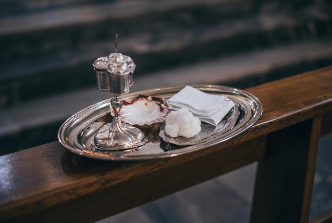 Srebrna taca z akcesoriami do chrztu: muszla, wacik i lniana serwetka, ustawiona na drewnianej ławce w kościele.