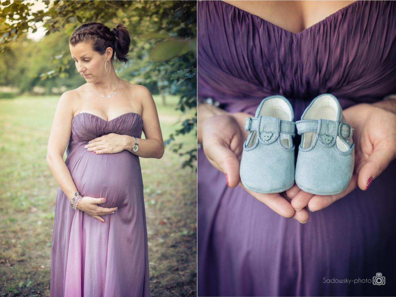 Kobieta w fioletowej sukni ciążowej trzymająca w dłoniach parę błękitnych bucików dla niemowląt na tle zieleni.