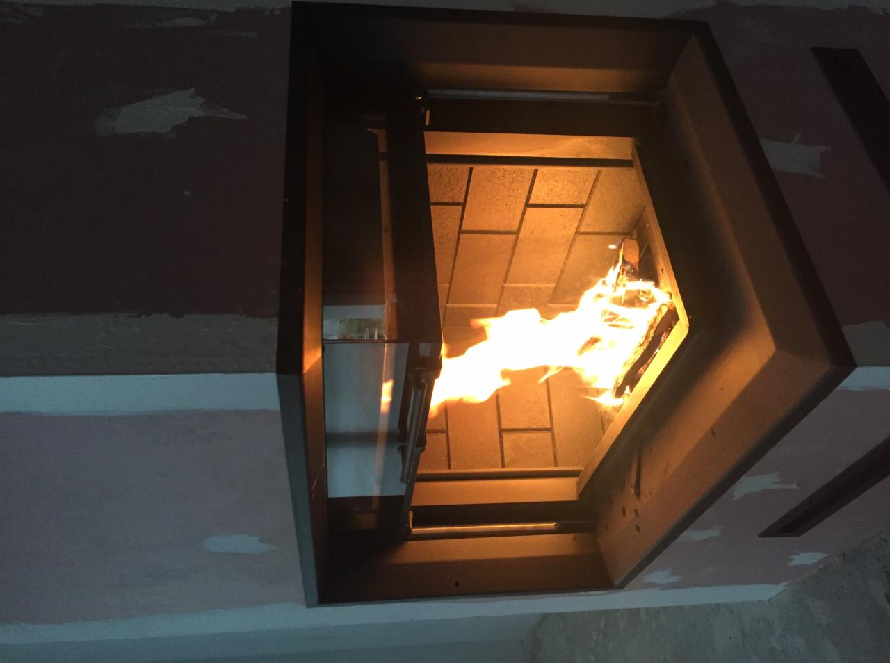 Otwarty, nowoczesny kominek z palącym się drewnem, widok z dołu na ceglane wnętrze paleniska.