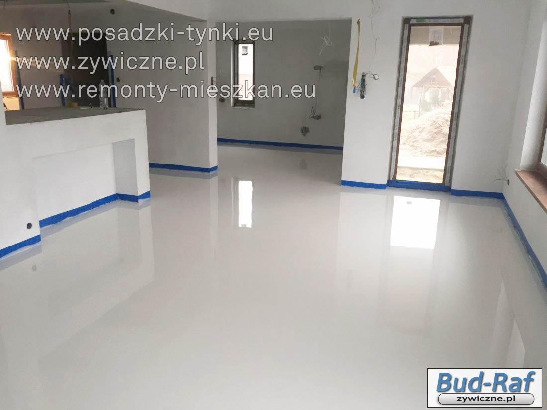 Biała, błyszcząca podłoga żywiczna w pomieszczeniu w trakcie prac wykończeniowych w Nasielsku, zabezpieczona niebieską taśmą malarską przy ścianach i framugach drzwiowych.