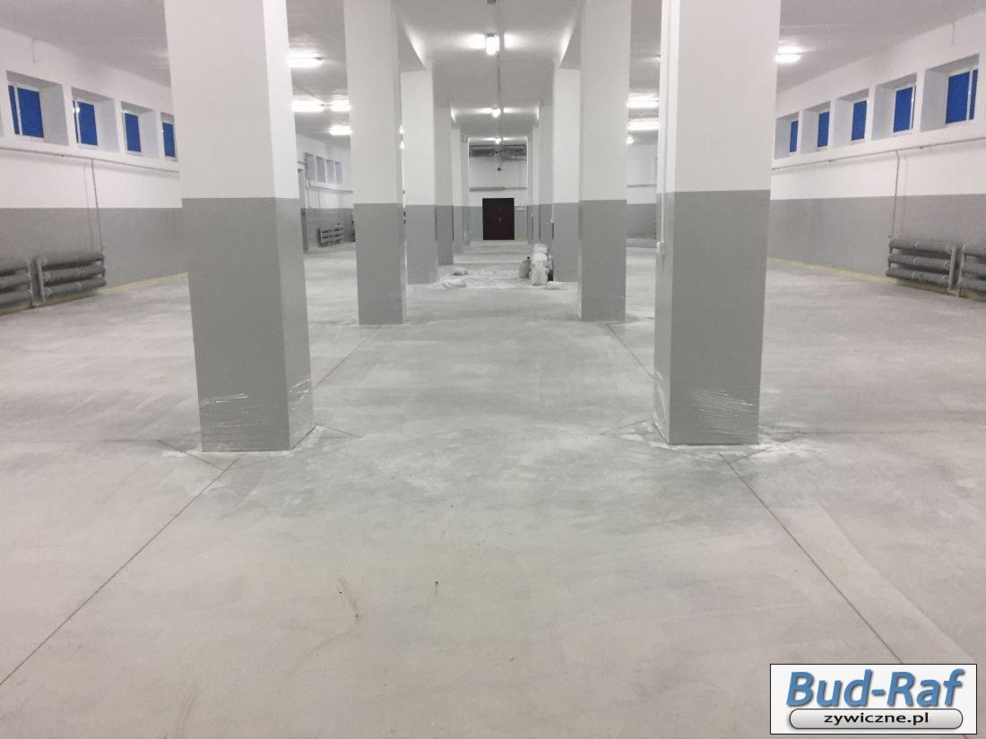 Przygotowanie podłoża pod posadzkę w hali: szlifowanie betonu, zabezpieczone folią kolumny, widoczne ślady po szlifowaniu.