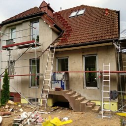 Bestdekarz Sp. z o.o. - Dom w trakcie ocieplania elewacji z rusztowaniami, widoczne materiały izolacyjne i drabiny. Na dachu zamontowane stopnie kominiarskie.