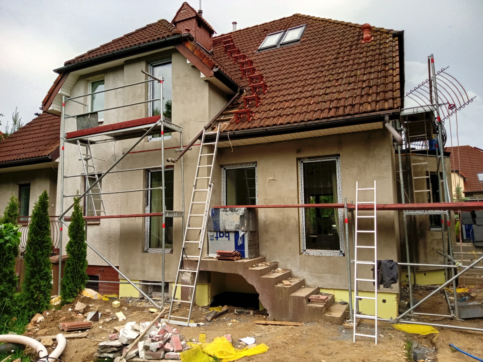 Dom w trakcie ocieplania elewacji z rusztowaniami, widoczne materiały izolacyjne i drabiny. Na dachu zamontowane stopnie kominiarskie.