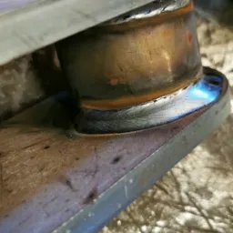 Spoina łącząca metalowy pierścień z płaskownikiem, widoczne przebarwienia termiczne i ślady obróbki.