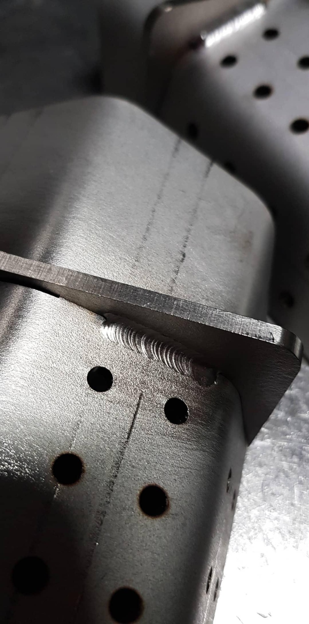 Metalowy element konstrukcyjny z widocznym spoiną i otworami, wykonany z blachy o szlifowanej powierzchni.