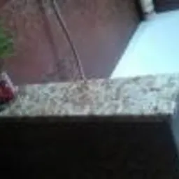 Fragment blatu o jasnej, ziarnistej fakturze, widoczny z perspektywy narożnika, z rośliną w tle i słabym oświetleniem.