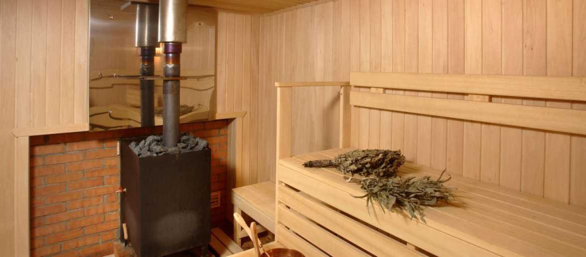 Wnętrze sauny z piecem opalanym kamieniami, drewnianymi ławkami i brzozowymi witkami.