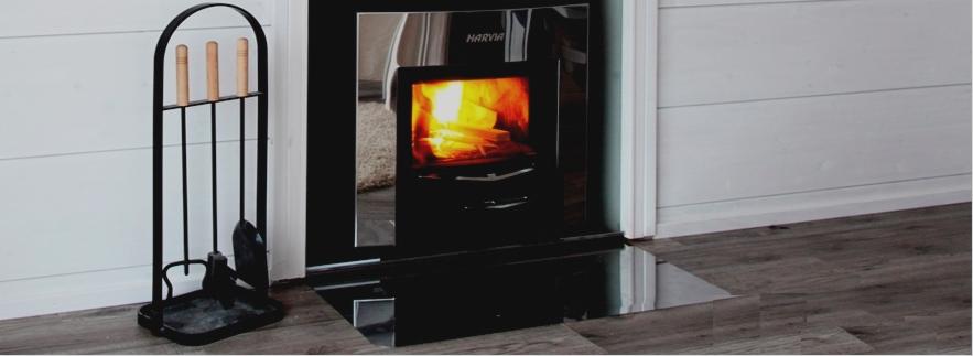 Opał w nowoczesnym, czarnym piecu kominkowym Harvia, obok zestaw narzędzi kominkowych z drewnianymi uchwytami.