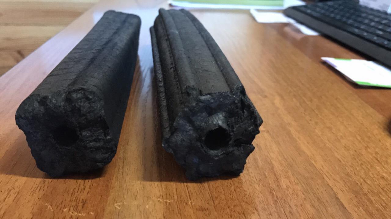 Dwa brykiety drzewne Pini Kay o cylindrycznym kształcie z otworem w środku, leżące na drewnianym biurku z widoczną klawiaturą w tle.