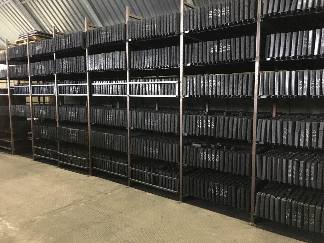 Magazyn z ułożonymi rzędami kostek aglomerowanego węgla drzewnego Pini Kay na metalowych regałach. Na każdym elemencie widoczne białe, naniesione numery.