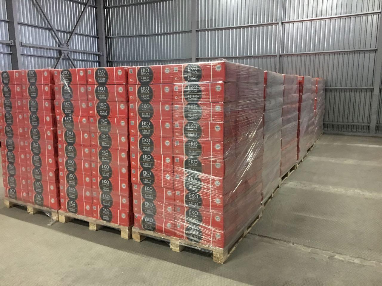 Magazyn z paletami zapakowanych w folię paczek z brykietem do grilla EKO MANGAL, widoczne metalowe elementy konstrukcji hali.