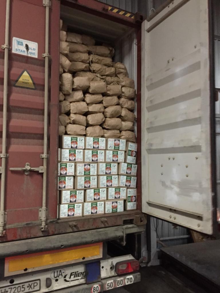 Otwarty kontener transportowy załadowany workami i kartonami z towarem, prawdopodobnie opałem, widoczne oznaczenia ostrzegawcze na kontenerze i tablica rejestracyjna pojazdu.