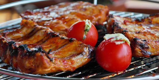 Grillowane żeberka z pomidorami nadziewanymi ziołami na ruszcie, widoczne przypalenia na mięsie.