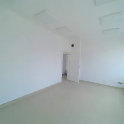 Puste, odnowione pomieszczenie z białymi ścianami, szarymi panelami sufitowymi i otwartymi białymi drzwiami prowadzącymi do innego pokoju z widoczną drabiną.