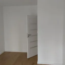 Pomalowane na biało wnętrze z panelami podłogowymi i otwartymi, białymi drzwiami z poziomymi przeszkleniami.