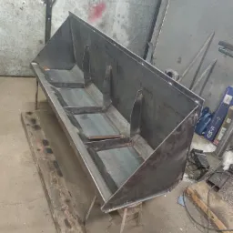 Metalowa konstrukcja z trzema komorami, spawana z blachy, na niskich nogach, prawdopodobnie na potrzeby rolnictwa, w warsztacie z widocznymi śladami obróbki.