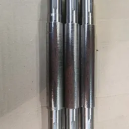 Trzy metalowe wałki z gwintowanymi końcówkami, ułożone pionowo na szarym tle. Środkowa część dwóch wałków ma ciemniejszy, rdzawy odcień, podczas gdy trzeci wałek jest w całości srebrny. Na wałkach...