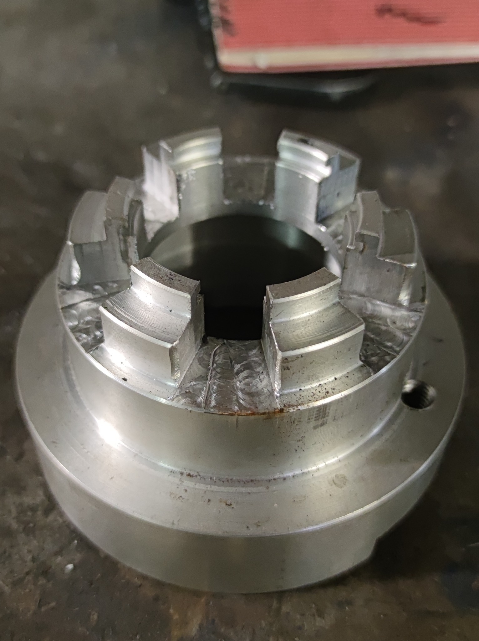 Metalowy element z wyfrezowanymi rowkami i śladami obróbki, widoczne zadrapania i nierówności powierzchni