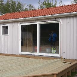 Bygg service - Budowa altany z drewnianym tarasem na zewnątrz, widoczny pracownik w środku przez przesuwne drzwi.