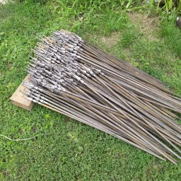 Ad- Mat - Wiele metalowych prętów z ozdobnymi grotami, ułożonych na trawie i drewnianym klocku. Elementy do balustrady lub bramy wjazdowej, przygotowane do montażu.