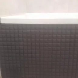 Obudowa wanny wykończona ciemną, kwadratową mozaiką z białym blatem, widoczny fragment ściany z jasnymi płytkami.