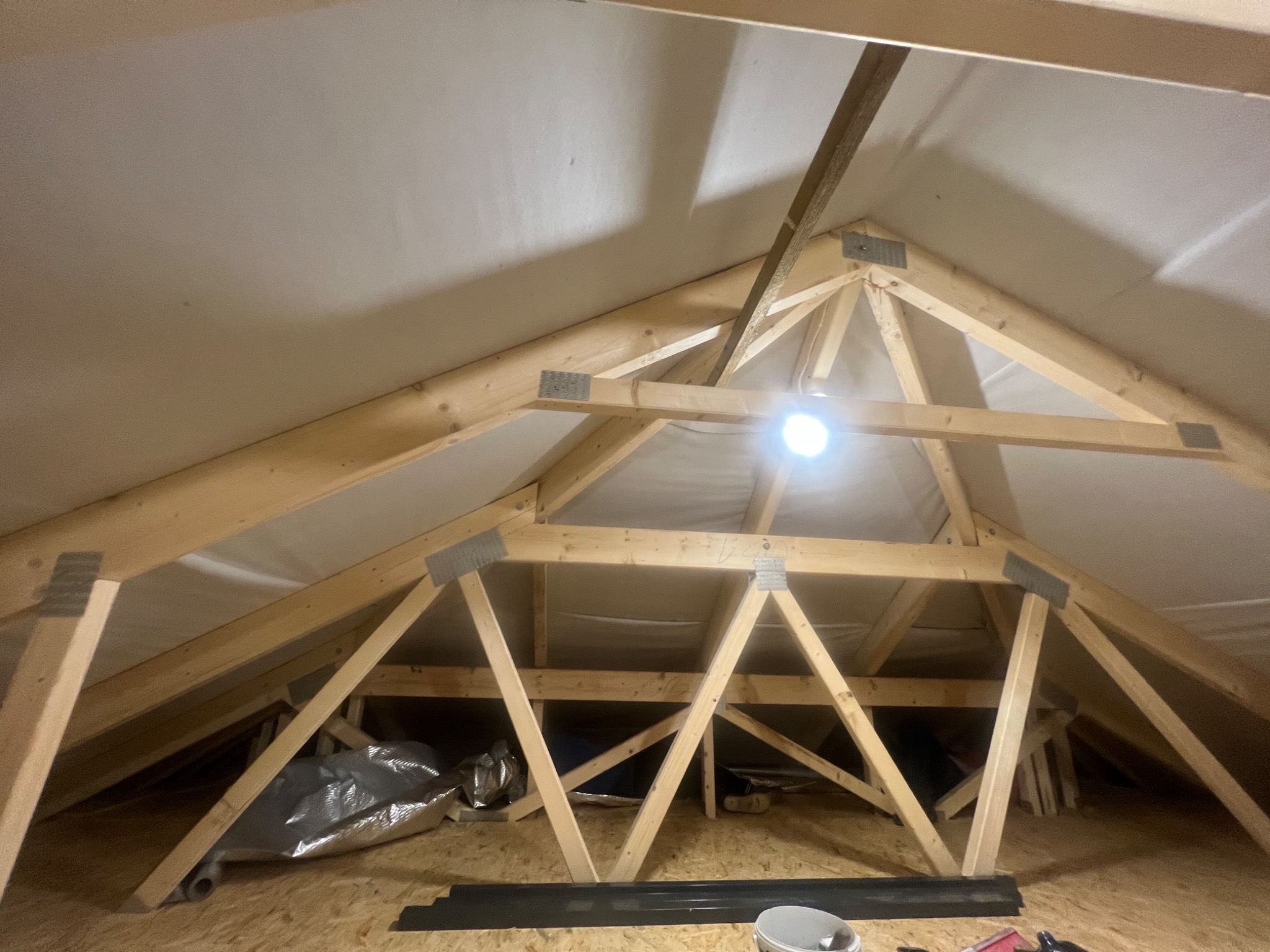 Poddasze z widoczną konstrukcją drewnianą, ocieplone od wewnątrz, z widocznym oświetleniem punktowym i elementami składowanymi na podłodze.