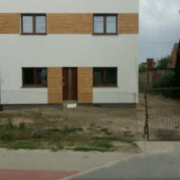 Dwukondygnacyjny budynek z białymi ścianami i poziomymi panelami imitującymi drewno, widok z ulicy, pochmurne niebo.