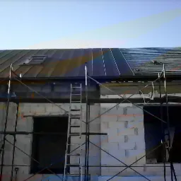 Budynek w trakcie budowy z częściowo położonym dachem z blachy trapezowej, widoczne rusztowania i drabina, okno dachowe.