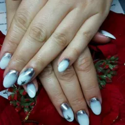 Dłonie z białymi paznokciami z efektem ombre przechodzącym w srebrny brokat na końcach, jeden paznokieć ozdobiony czarną gwiazdką, ułożone na czerwonej dekoracji świątecznej i ulotkach reklamowych.