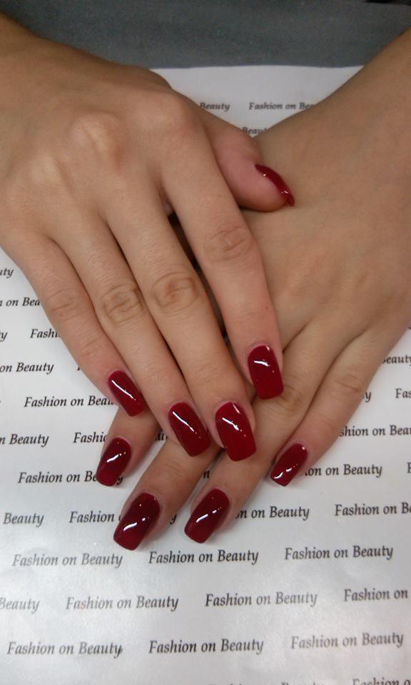 Dłonie z ciemnoczerwonym manicurem żelowym na tle papieru z napisem 'Fashion on Beauty'.