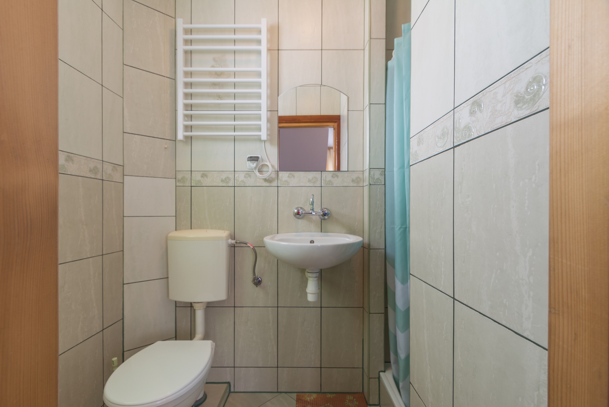 Jasna łazienka w Zakopanem z beżowymi płytkami, umywalką, toaletą i grzejnikiem drabinkowym.