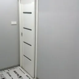 Zainstalowane białe drzwi przesuwne z czterema poziomymi wstawkami, widoczne zabezpieczenie podłogi folią ochronną z logo producenta.