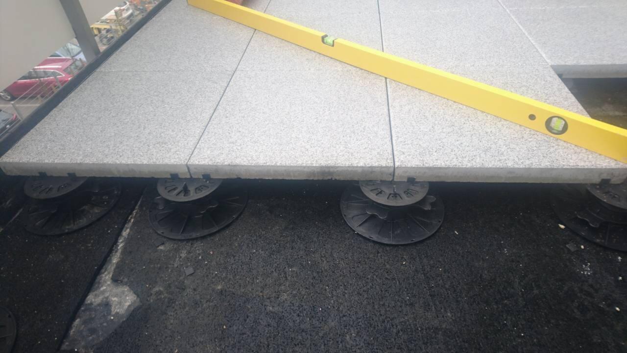 Montaż tarasu z płyt betonowych na regulowanych wspornikach, poziomowany żółtą poziomicą.