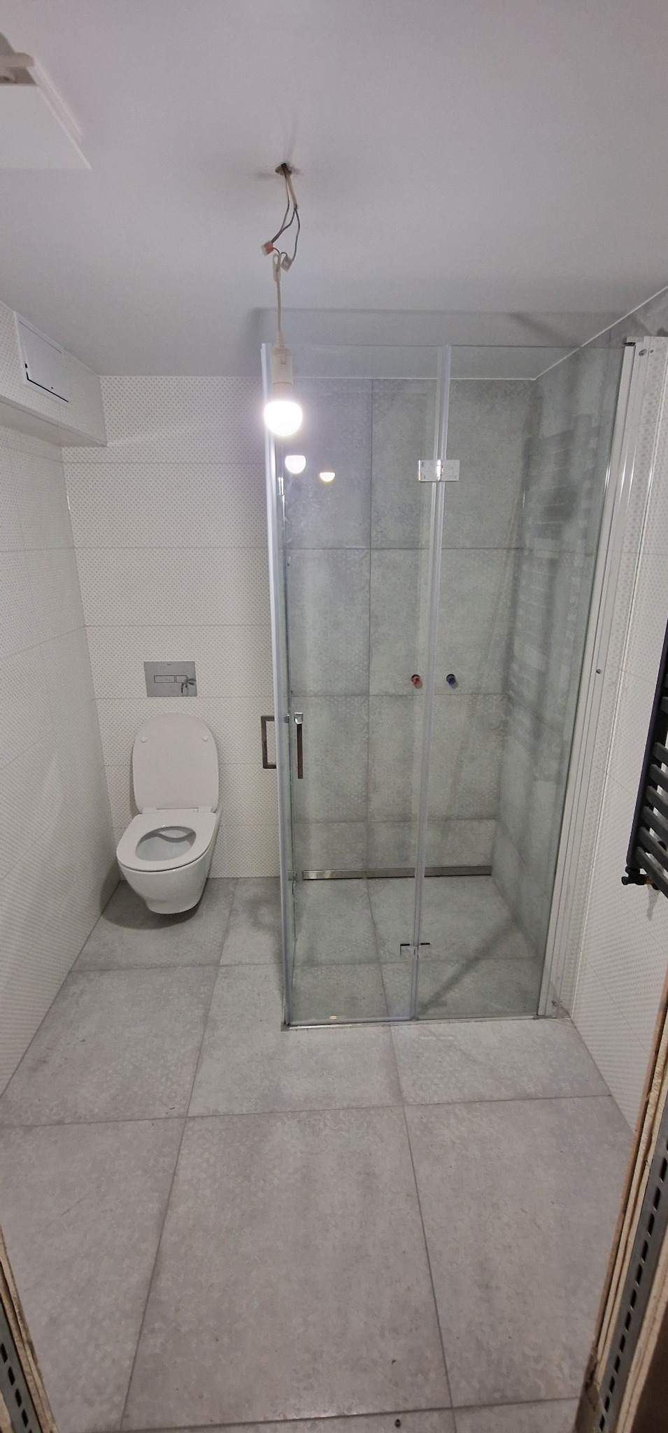 Nowoczesna łazienka w Łodzi z kabiną prysznicową ze szklanymi drzwiami, wiszącą toaletą z podtynkowym systemem spłukiwania i szarymi płytkami podłogowymi oraz ściennymi z delikatnym wzorem...