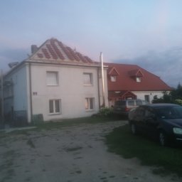 MAT-WOOD - Dwupiętrowy dom z częściowo wymienionym pokryciem dachowym z czerwonej dachówki, widoczne rusztowania i zaparkowane samochody na posesji.