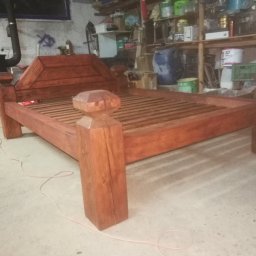 MAT-WOOD - Drewniane łóżko w surowym wnętrzu warsztatu, z widoczną strukturą drewna i prostym zagłówkiem. W tle półki z narzędziami i farbami.