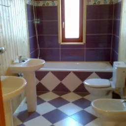 Wnętrze wykończonej łazienki z drewnianą boazerią, fioletowymi płytkami na ścianach i podłodze ułożonej w romby, z wanną, toaletą, bidetem i dwiema umywalkami na postumentach.