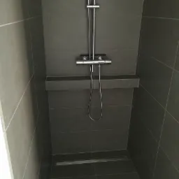 Nowoczesny prysznic z szarymi płytkami, chromowaną armaturą i odpływem liniowym w podłodze, widok z góry.