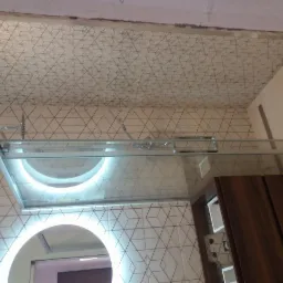 Nowoczesna łazienka z geometrycznymi płytkami na ścianach i suficie, oświetlonym lustrem i szklaną kabiną prysznicową z podświetleniem LED.