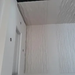 Nowoczesne wykończenie wnętrza: białe, teksturowane panele ścienne i sufitowe z motywem fal, oświetlenie punktowe w ścianie przy framudze drzwi.