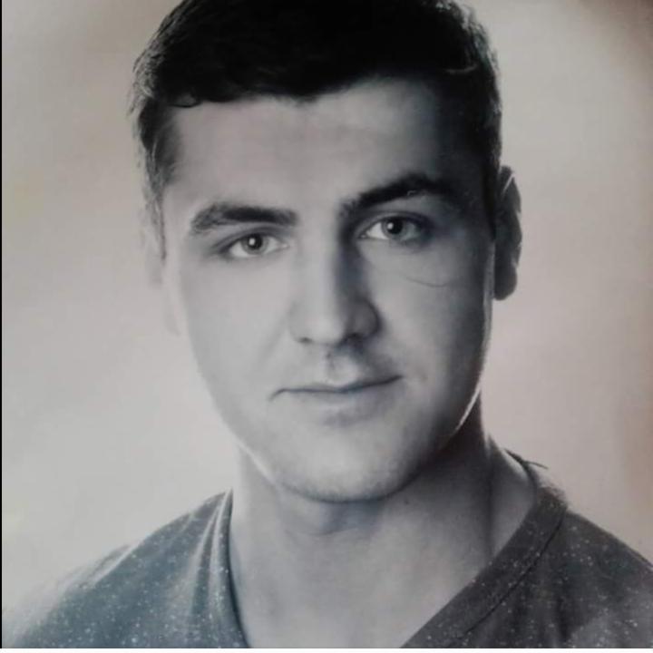 Czarno-biały portret młodego mężczyzny z krótkimi włosami i ciemną koszulką na jasnym tle. Ujęcie od przodu, skupione na twarzy i wyrazie oczu.