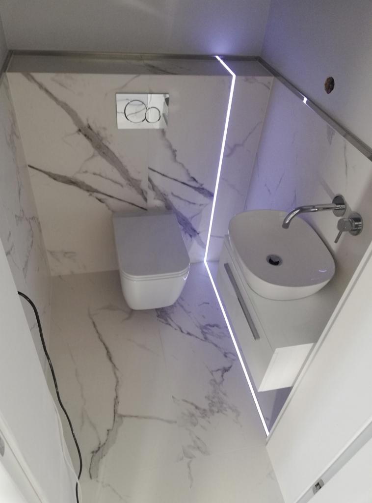 Nowoczesna łazienka w bieli i marmurze z podświetleniem LED, owalna umywalka nablatowa i podwieszana toaleta.