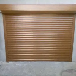 Zamknięta, brązowa osłona okienna z poziomych lameli, zamontowana na zewnątrz budynku z szarego betonu i cegieł.