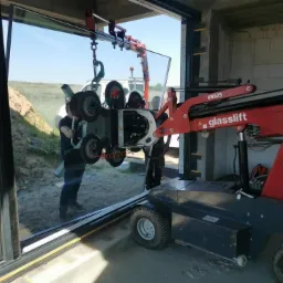 Montaż dużej szyby okiennej przy użyciu specjalistycznego podnośnika Glaslift w surowym stanie budynku.