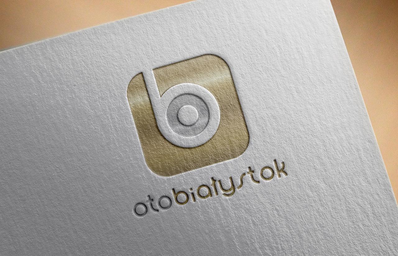 Logo 'otoBiałystok' z symbolem litery 'b' w zaokrąglonym kwadracie, wytłoczone na teksturowanym, białym papierze z elementami w kolorze złota.
